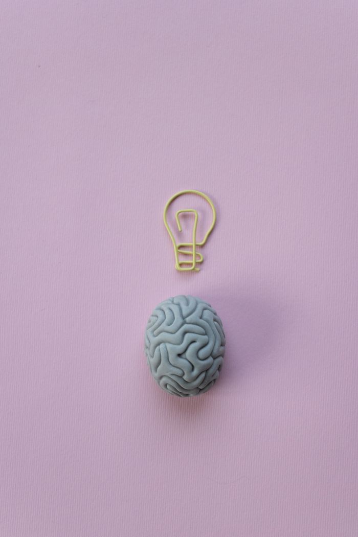 about-01 Brain-shaped eraser with a light bulb paperclip on a pastel pink background. Ideal for education and creativity themes.